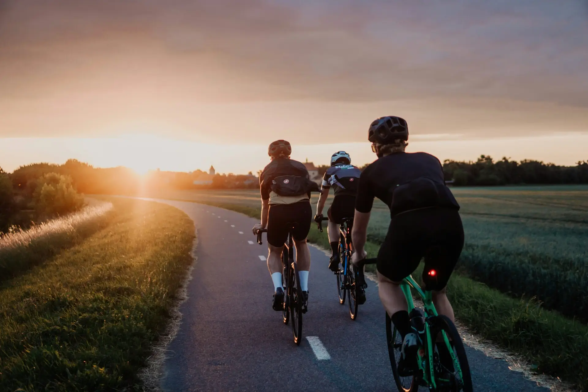 Groep wielrenners fietst over een landelijke fietsroute tijdens zonsondergang met goed onderhouden racefietsen.
